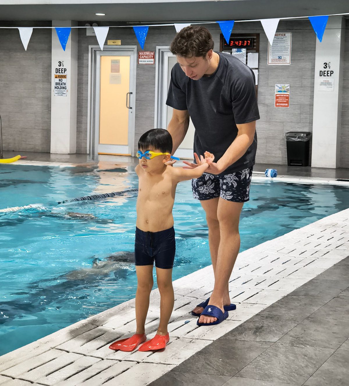 A Shark Swim coach guiding a young swimmer through arm position on the pool deck